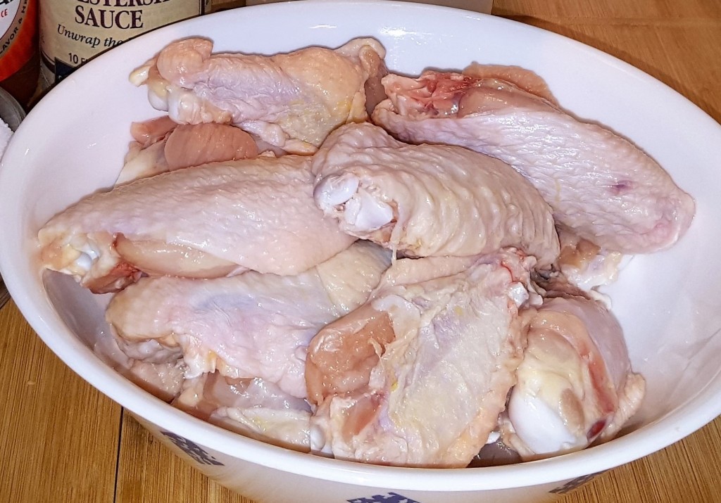 A round white plate with raw chicken wings in it.
