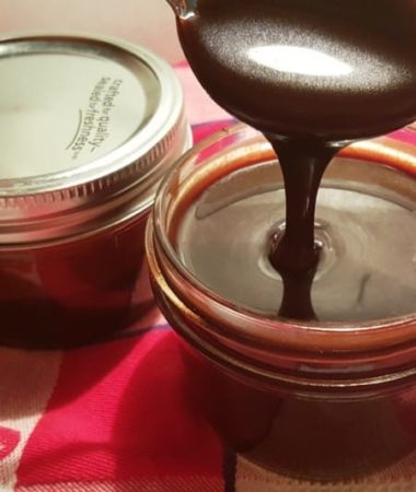 A mason jar with a spoon pouring the Hot Fudge Sauce