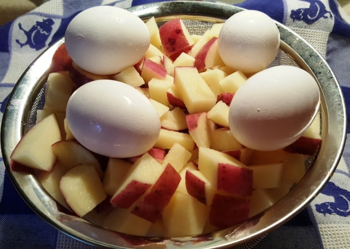 A strainer basket with boiled eggs and chopped potatoes