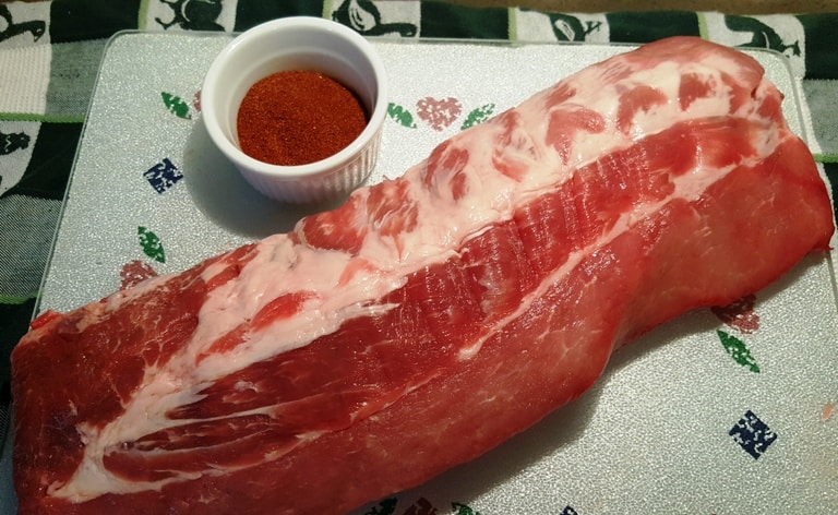A close up of raw pork ribs with a small bowl of barbeque ribs rub.