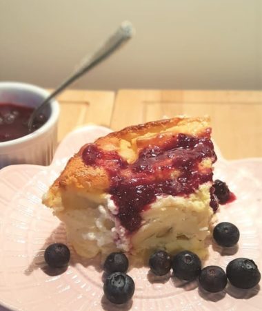 A portion of blintz souffle on a plate with sauce and blueberries