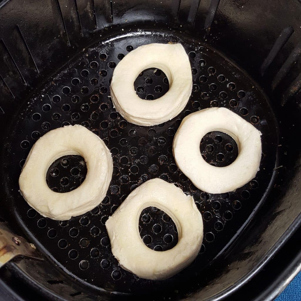 Four raw doughnuts inside of air fryer basket
