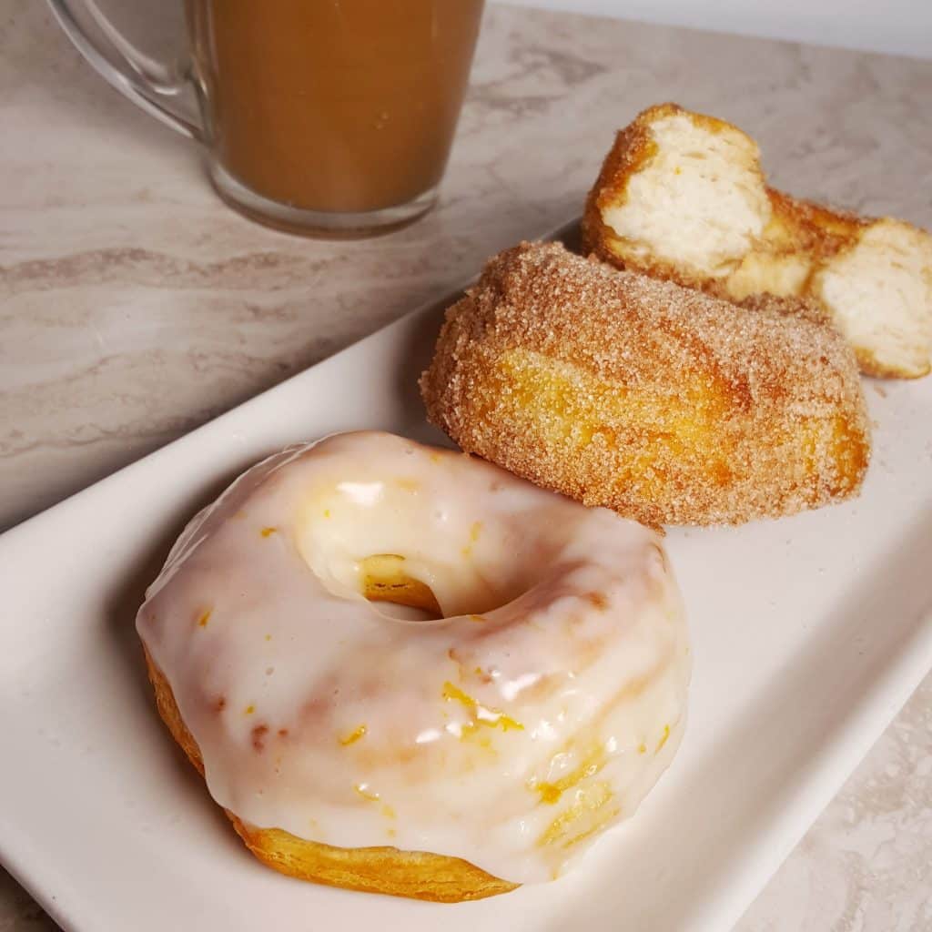 Vanilla and Chocolate Glazed & Cinnamon Sugar Doughnuts on a white plate with a cup of hot coffee.