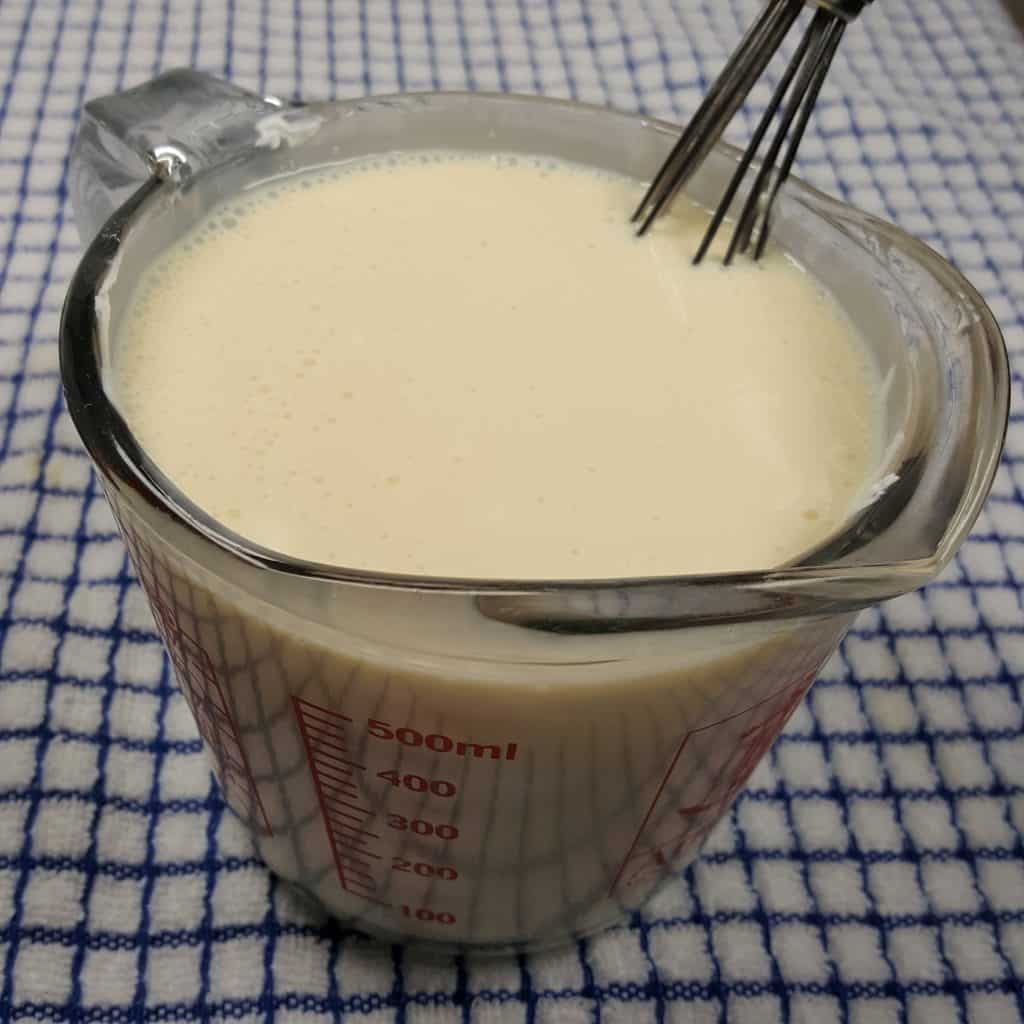 Sweetened Condensed Milk and Yogurt Cheese in a measuring jug with a whisk in it on a kitchen towel. 