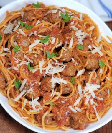 Big plate of spaghetti and meatballs on a white serving platter on a rustic wood table