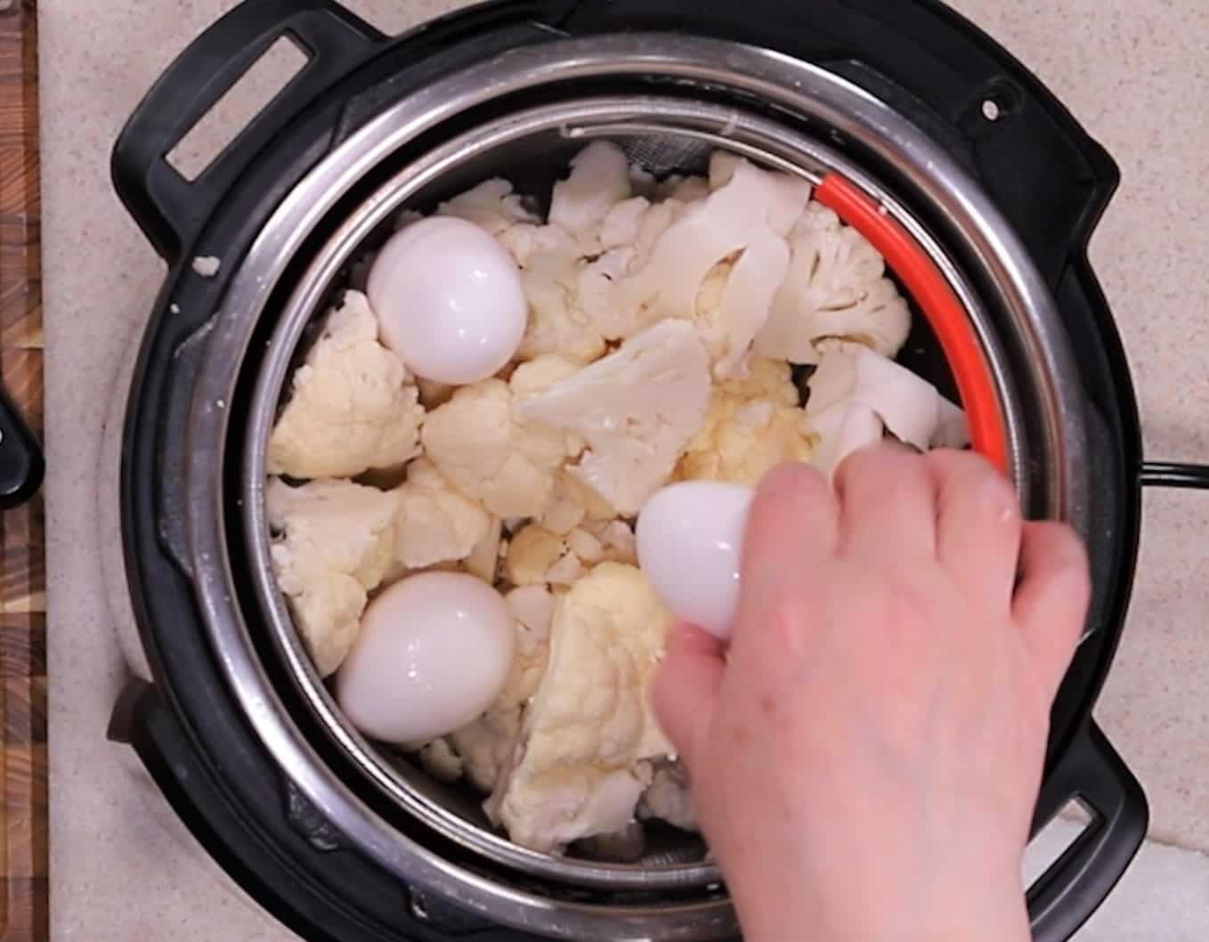 Raw eggs placed on top of cauliflower in basket in Instant Pot