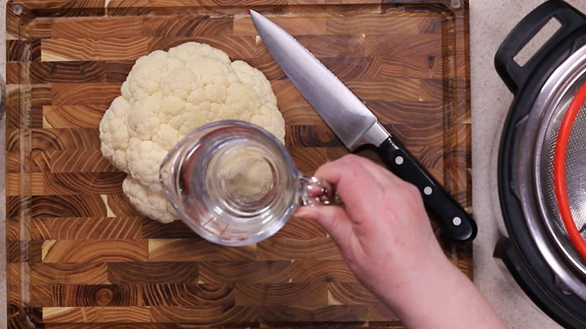 Head of Cauliflower Flower on a Cutting Board with Knife and a hand holding a glass of water.