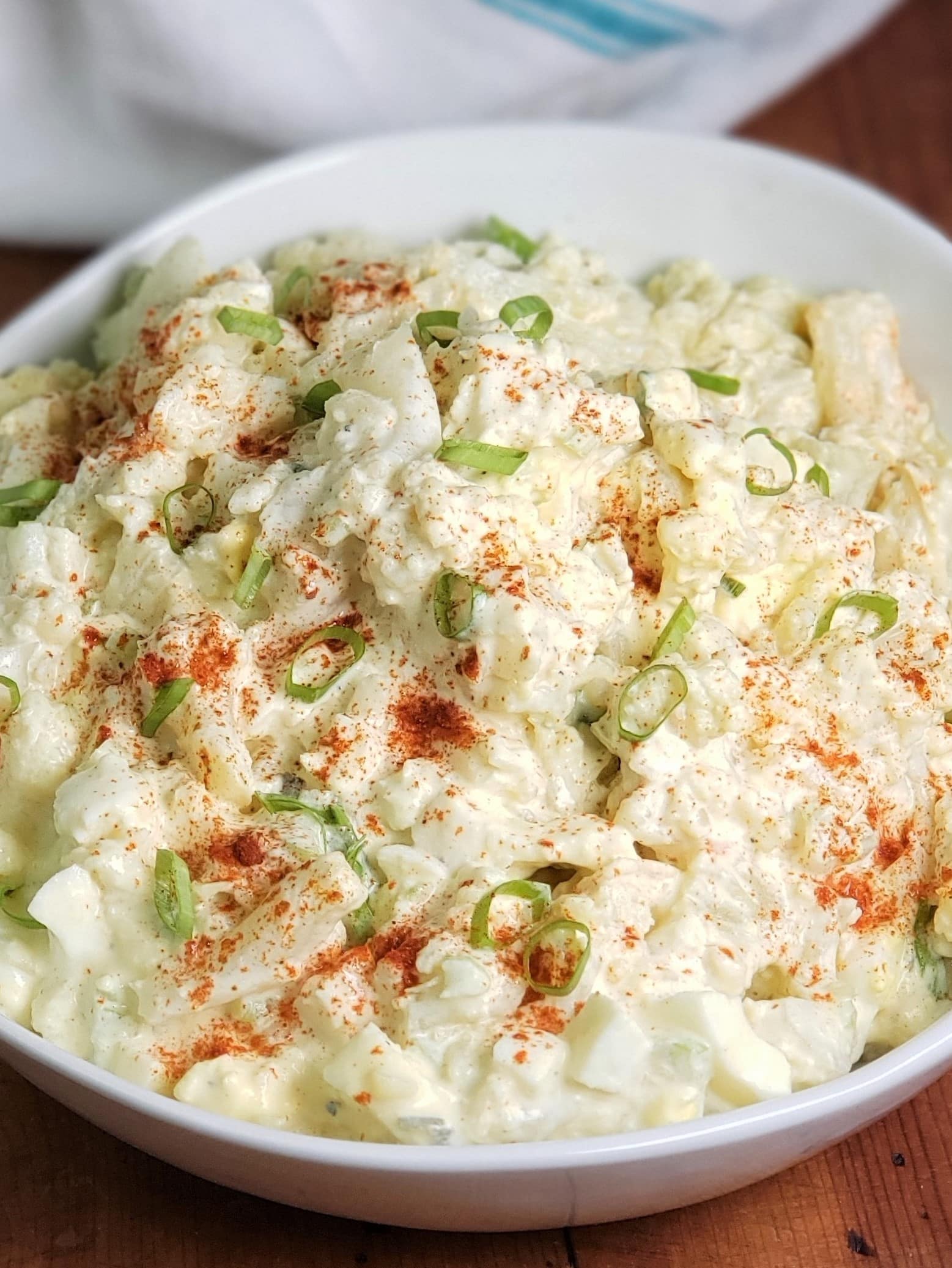 White Round Bowl with Cauliflower Mock Potato Salad, garnished with red paprika and green scallions for color