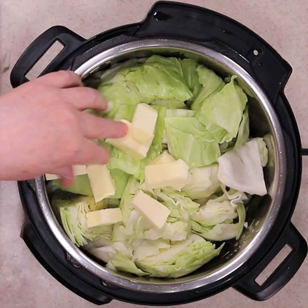 Sliced butter on top of green chopped cabbage in Instant Pot